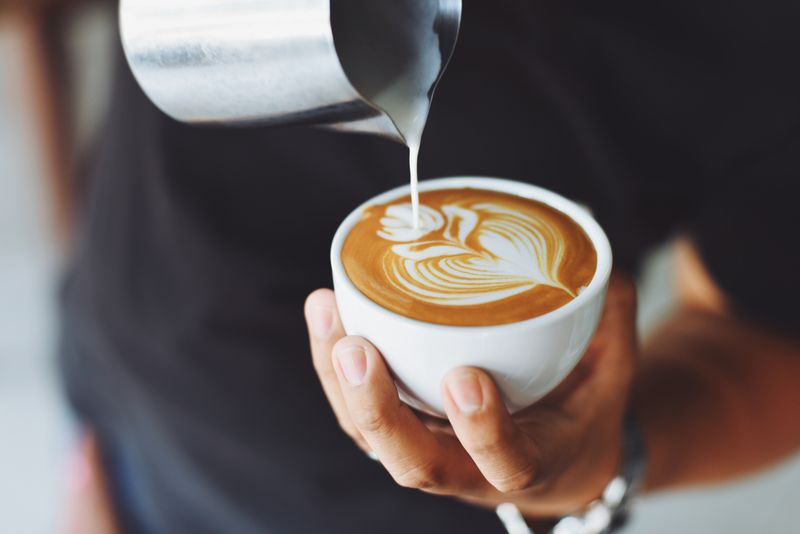 Barista sirviendo un capuchino con arte latte recién preparado